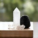 An artfully arranged cluster of tumbled crystals – selenite, black tourmaline, clear quartz – on a minimalist shelf in a sunlit room, promoting positive home energy.